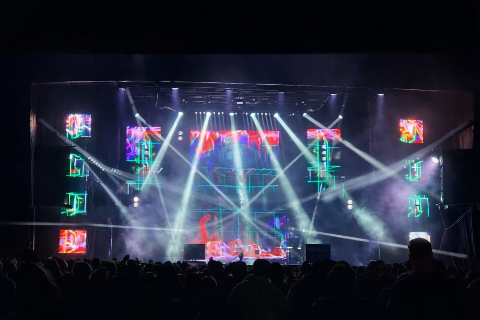 Escenario de conciertos con luces brillantes, una banda tocando y una multitud de personas en la oscuridad.