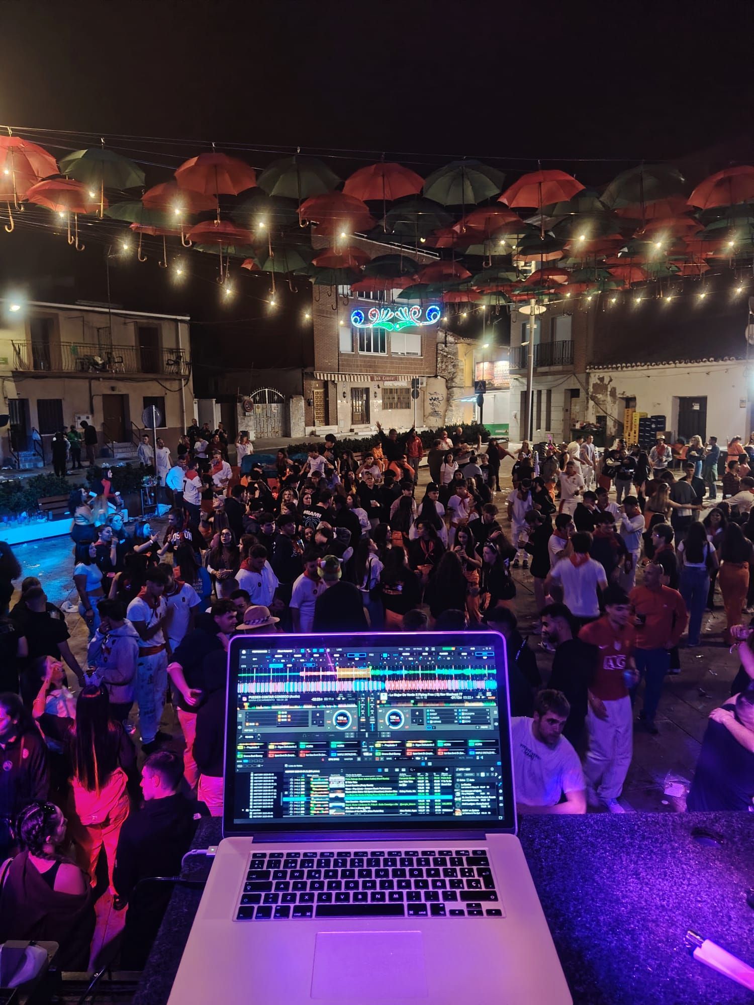 Configuración de DJ en una fiesta nocturna al aire libre. Público bailando bajo sombrillas colgantes y guirnaldas de luces.