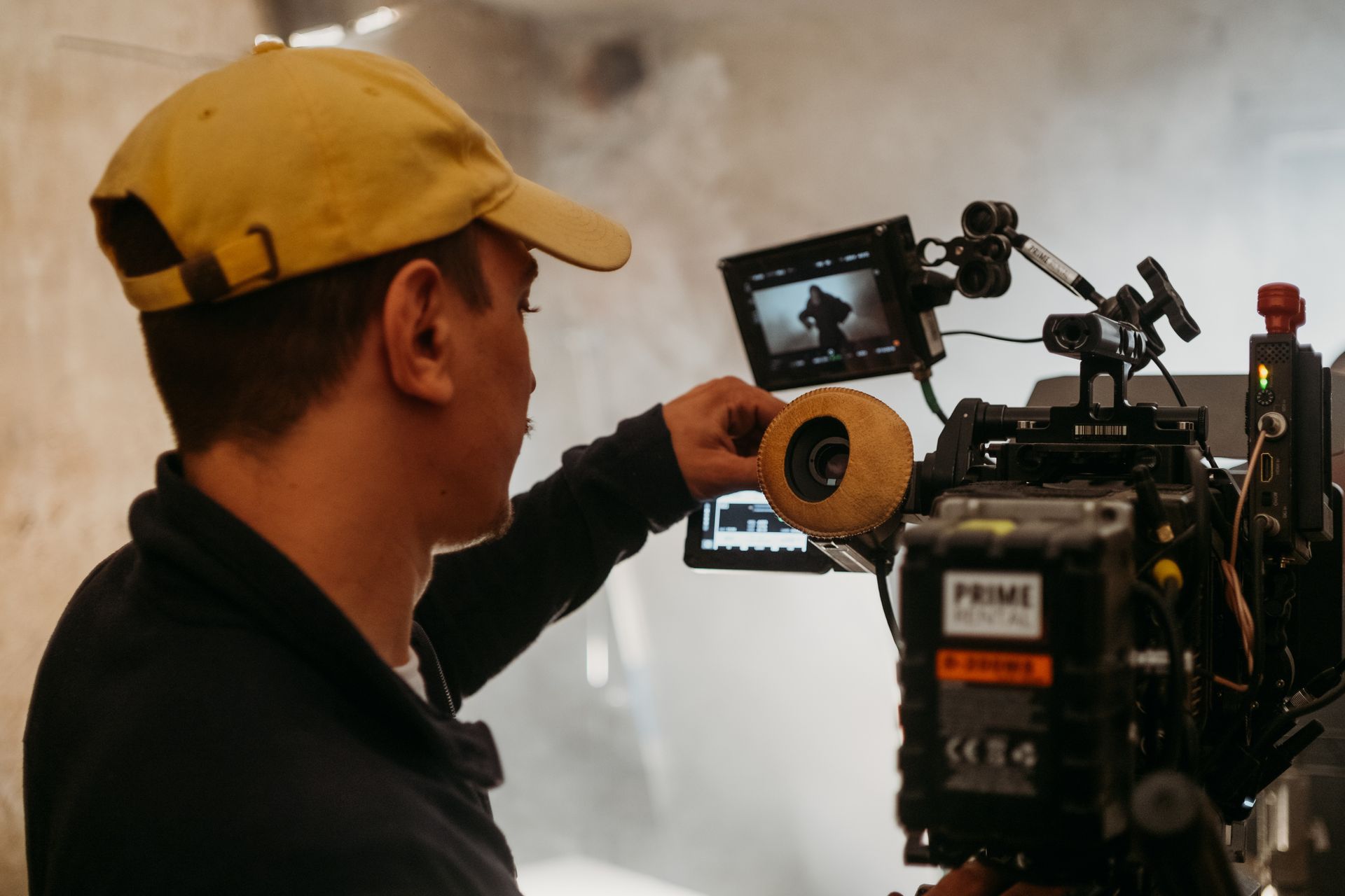 Hombre con gorra amarilla operando una cámara profesional en un set lleno de humo.