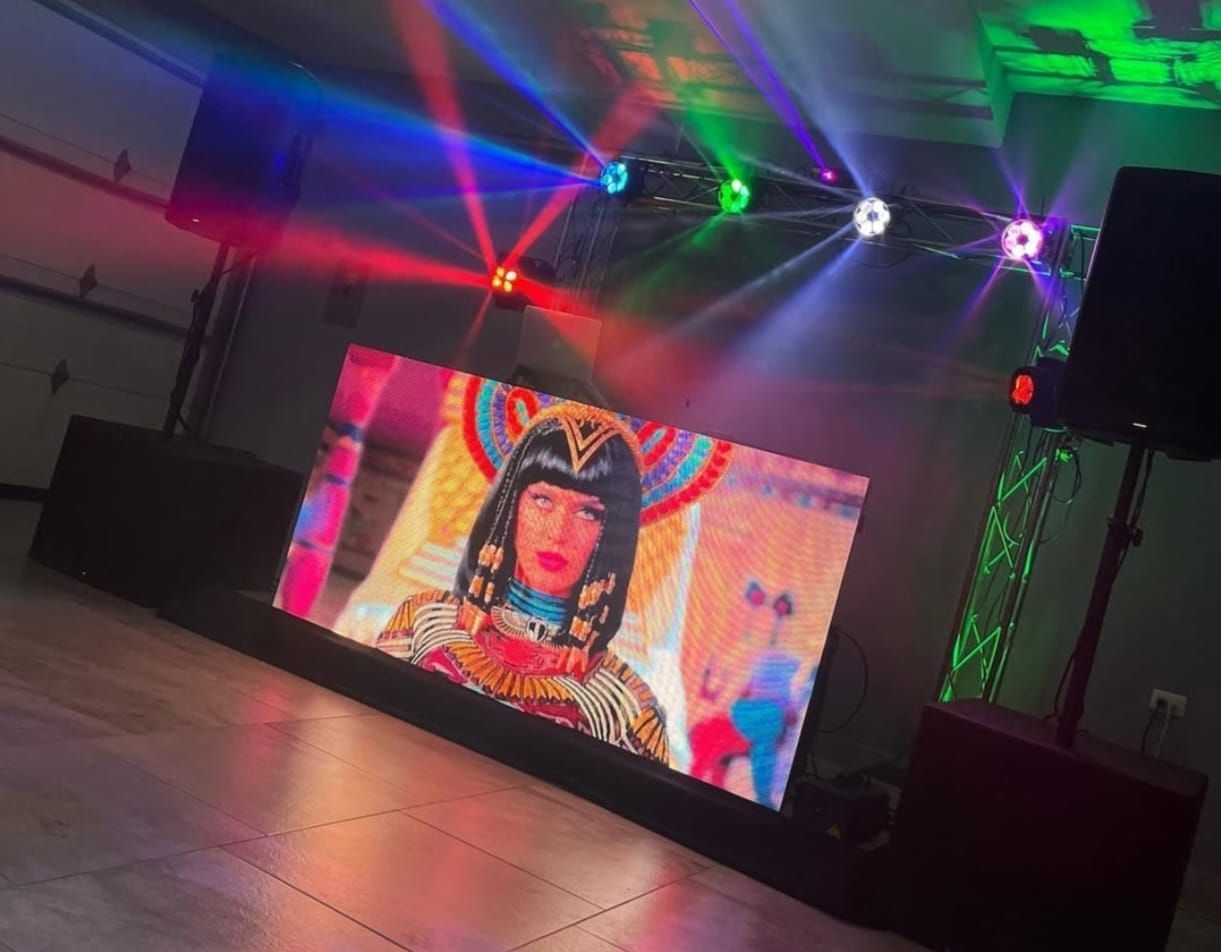 Configuración de DJ con una pantalla grande que muestra una imagen, luces de escenario y altavoces.