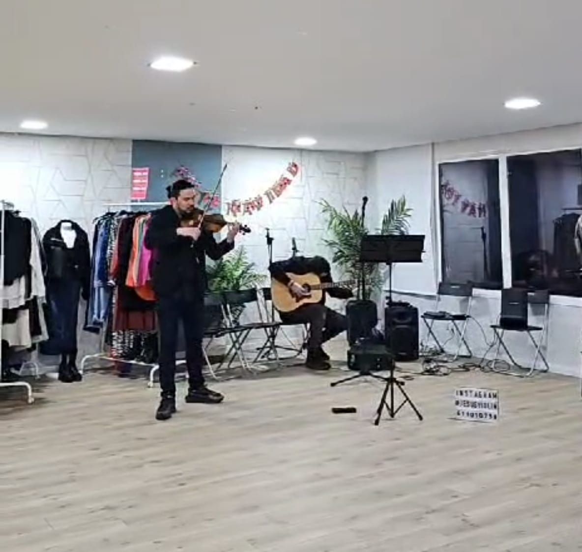 Músicos tocando en una sala. Un violinista toca mientras un guitarrista los acompaña. Un perchero al fondo.