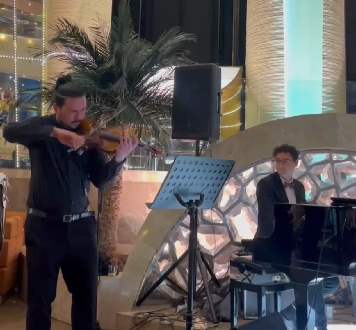 Dos músicos interpretando: un violinista y un pianista en un local. El violinista toca, el pianista al piano. Interior moderno.