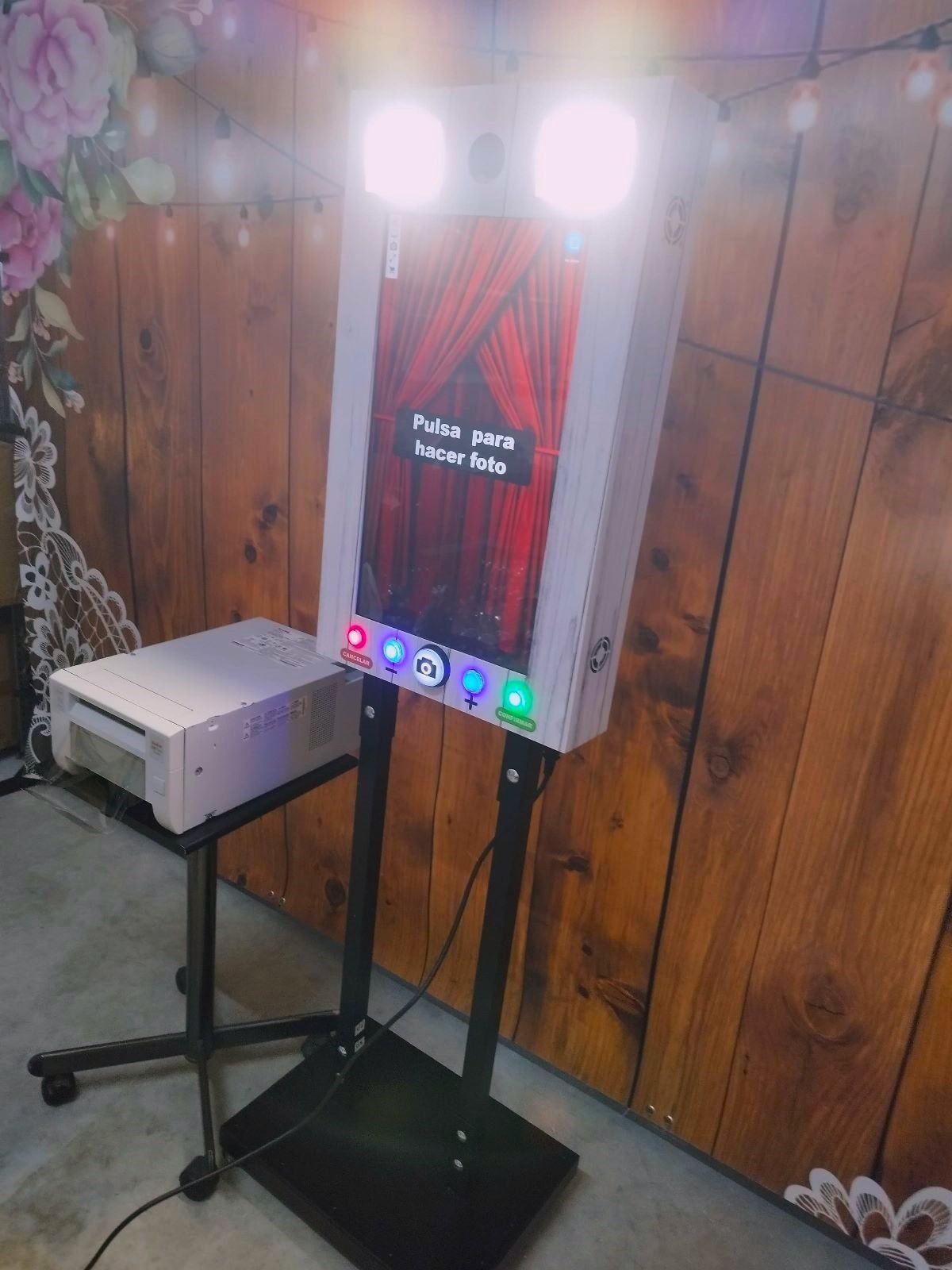 Fotomatón con impresora sobre soporte, fondo de madera y luces.