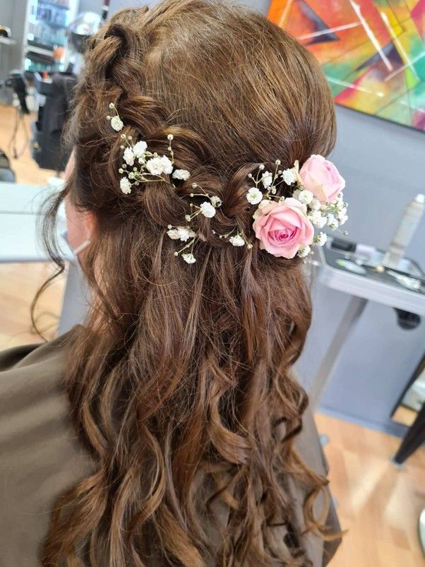 Eine Frau trägt eine halb hochgesteckte, halb offene Frisur und hat Blumen im Haar.