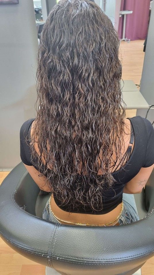 Eine Frau mit lockigem Haar sitzt in einem Salon auf einem Stuhl.