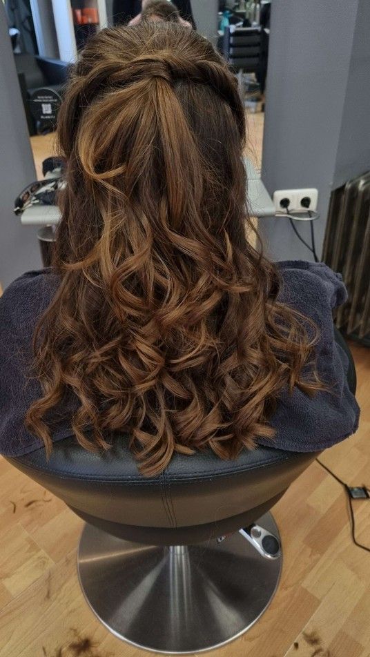 Eine Frau sitzt auf einem Stuhl und hat ihr Haar halb hochgesteckt und halb heruntergelassen.