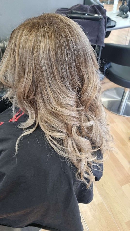 Eine Frau mit langen blonden Haaren sitzt in einem Salon auf einem Stuhl.