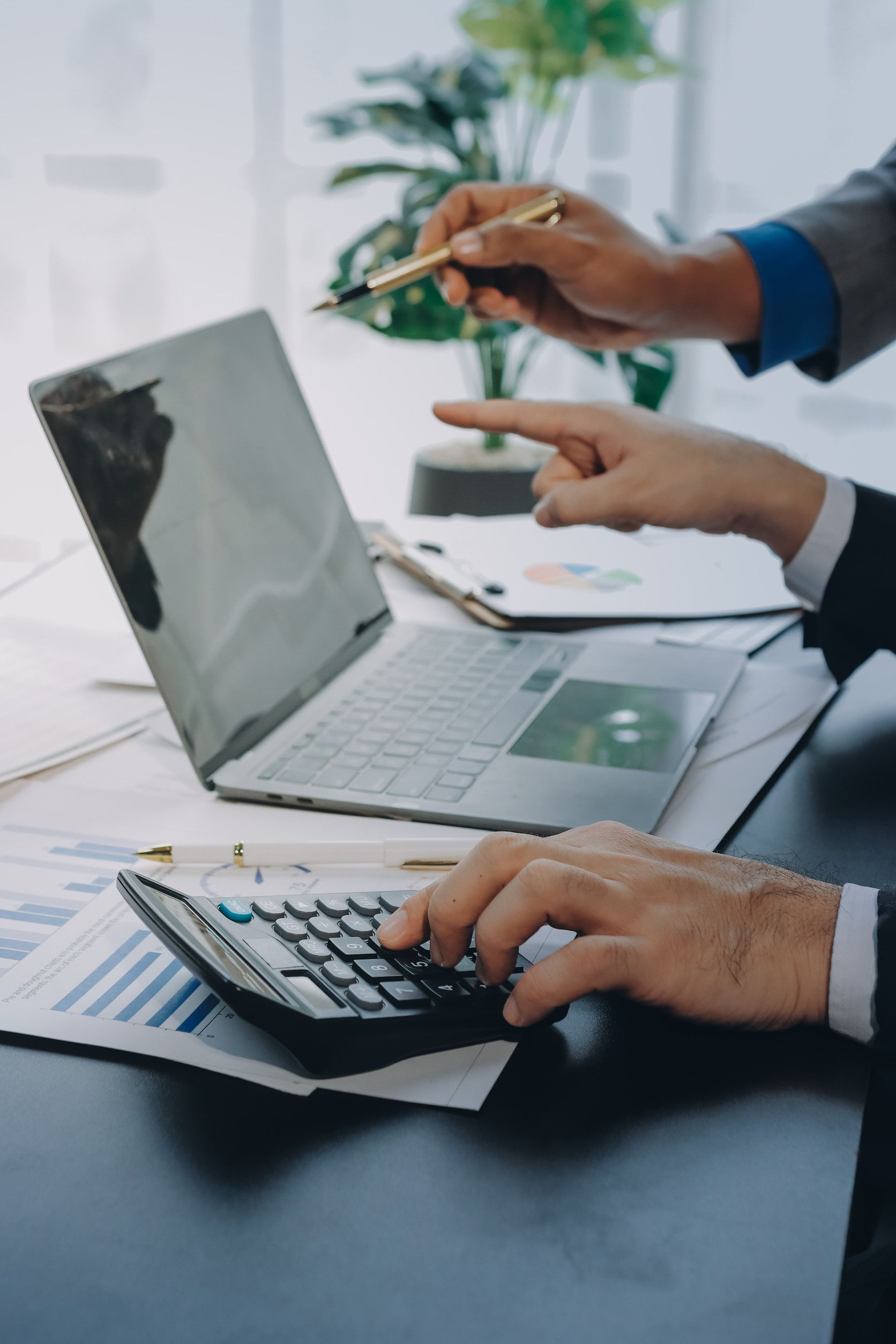Dos personas trabajan con una laptop, calculando con una calculadora. Una apunta con un bolígrafo y analiza datos.