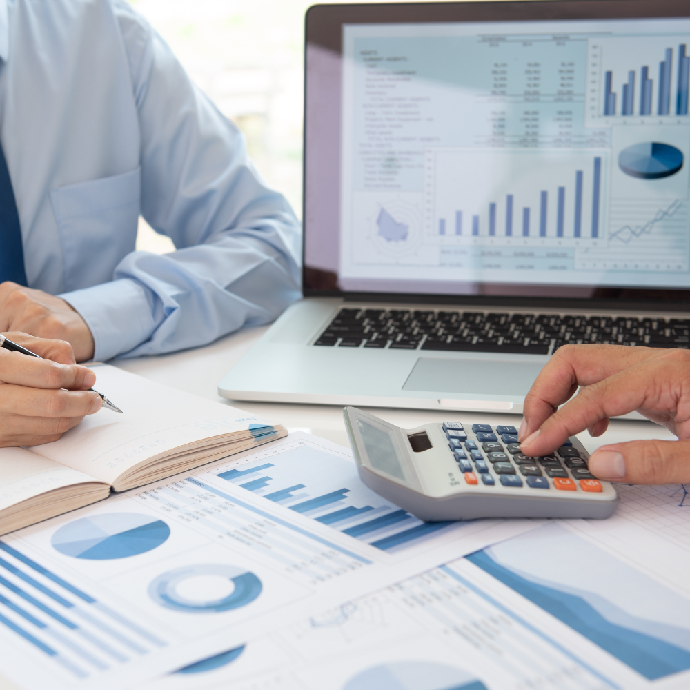 Dos personas revisan gráficos financieros con una computadora portátil y una calculadora, en un entorno de oficina.