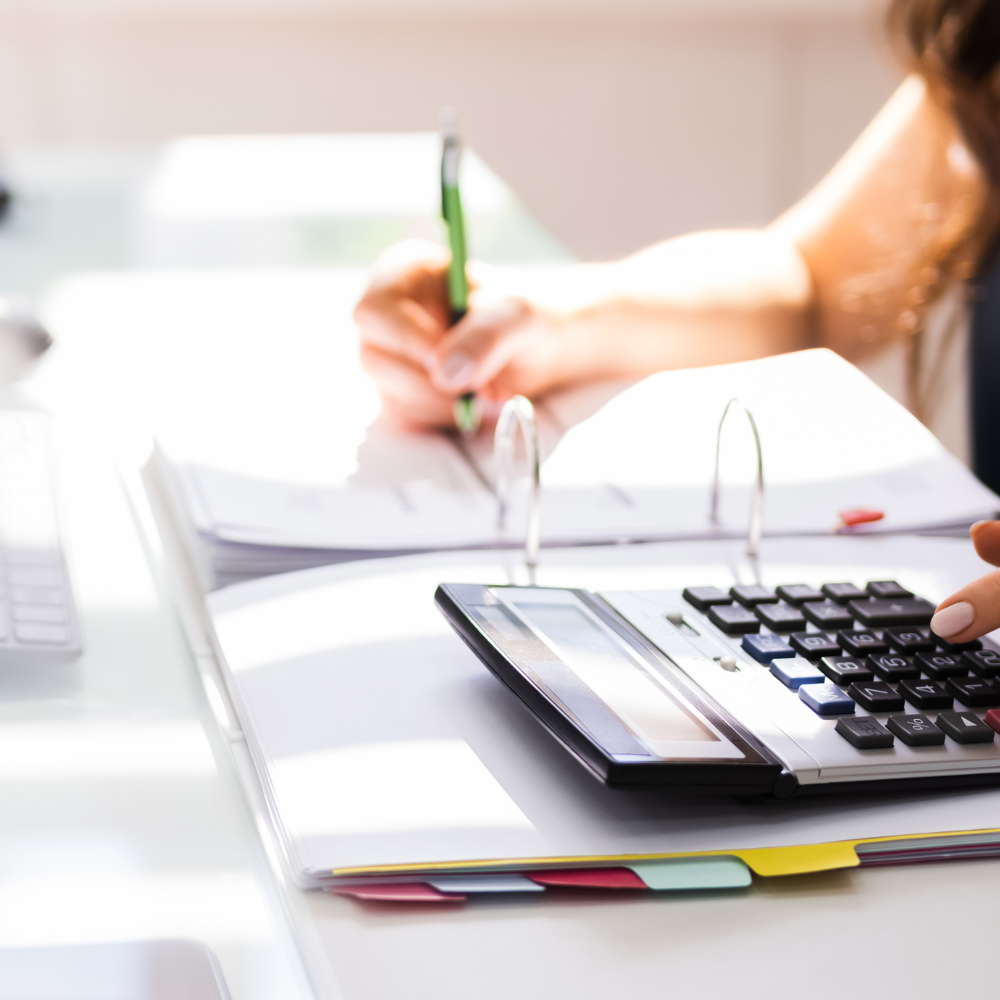 Mujer usando calculadora y escribiendo en papeles en un entorno de oficina.