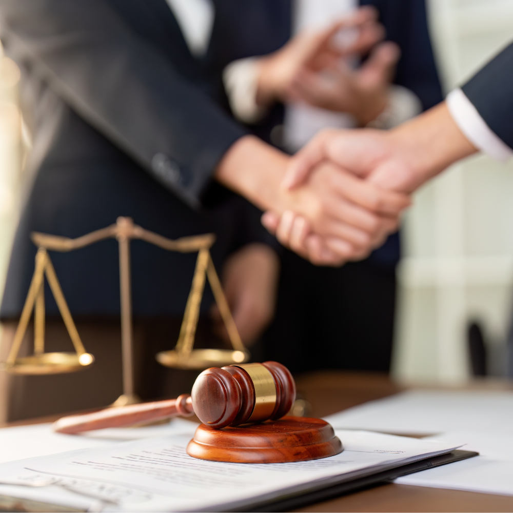 Personas se dan la mano frente a una balanza de justicia y un mazo sobre documentos legales.