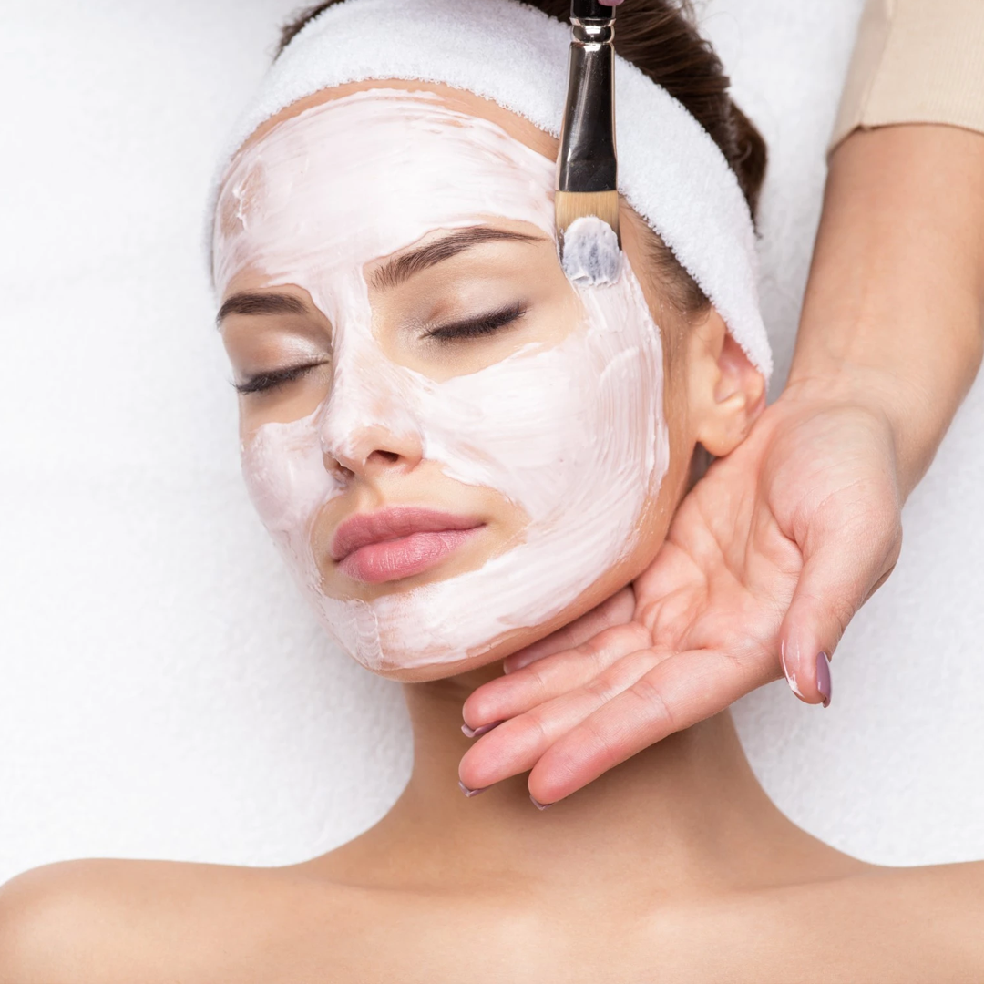 Donna che riceve l'applicazione di una maschera facciale. La maschera bianca viene applicata con un pennello.