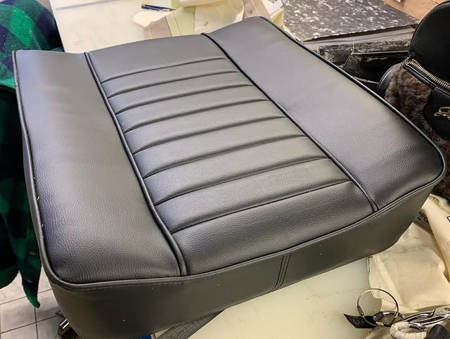 Coussin de siège auto en cuir noir avec panneau central côtelé et renforts latéraux, présenté sur un établi.