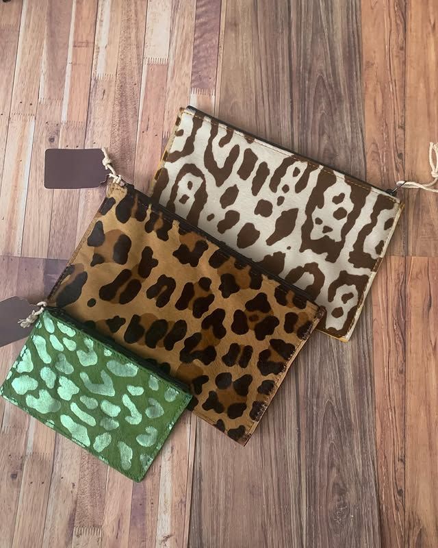 Trois pochettes à motifs verts, marrons et crème sur un parquet