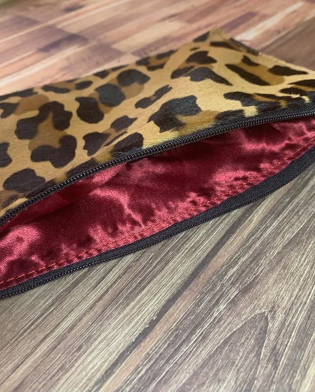 Pochette en tissu imprimé léopard avec doublure en satin rouge sur un sol en bois