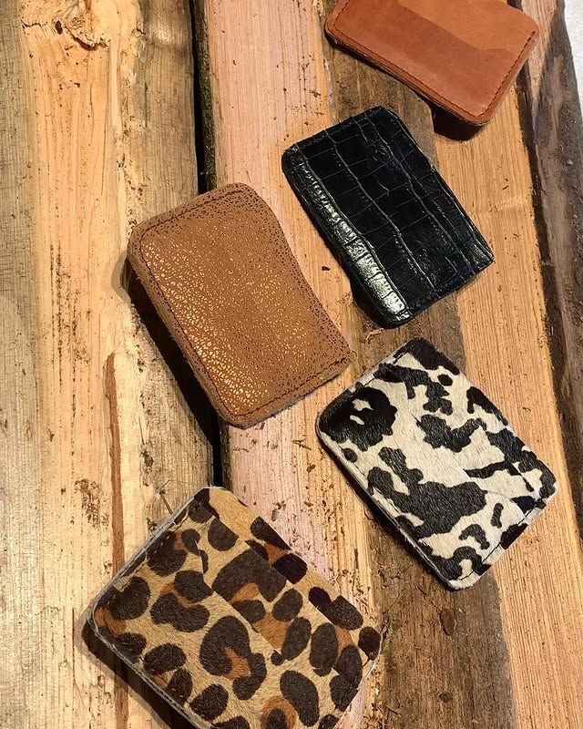Quatre petits portefeuilles en cuir à motifs, présentés sur une surface en bois, dans les tons beige, noir, crème et léopard.