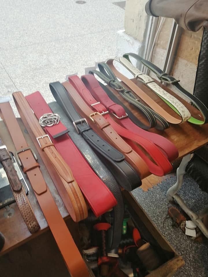 Des ceintures en cuir assorties, rouges, marron et noires, sont disposées sur une table de magasin près d'une porte.