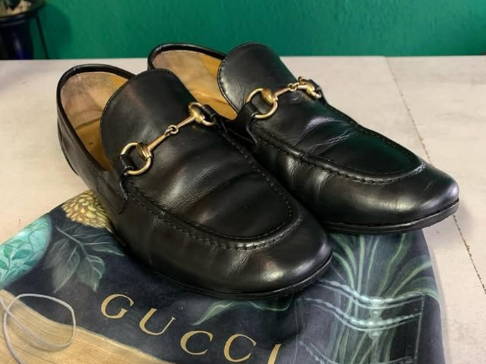 Mocassins Gucci noirs avec mors doré sur une boîte Gucci, présentés côte à côte.
