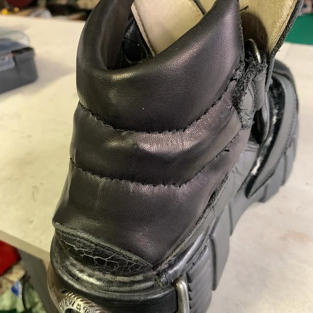 Gros plan sur le talon d'une botte noire, coutures et usure apparentes, posée sur un établi.