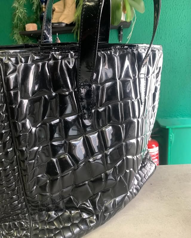 Sac cabas noir matelassé à anses tressées, posé sur une table devant un mur vert.