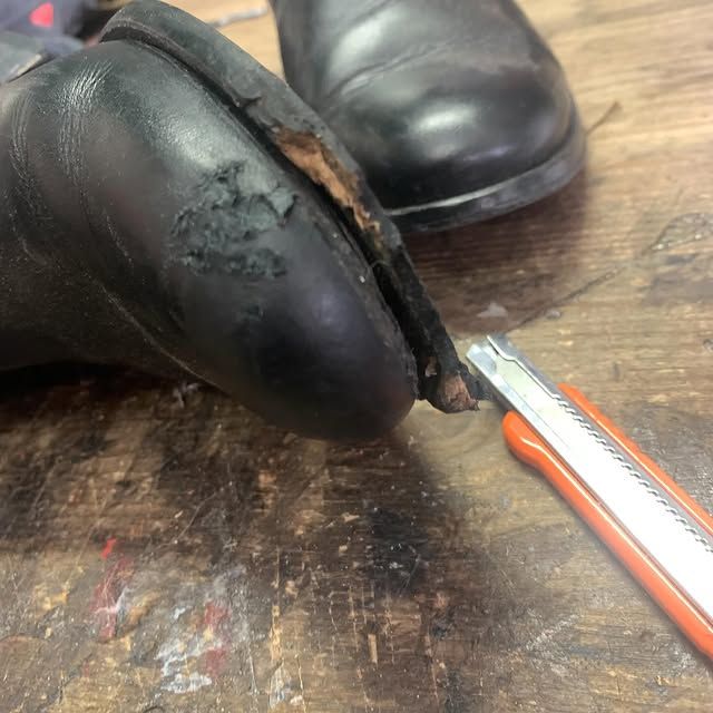 Une chaussure noire est découpée au cutter sur une surface en bois usée.