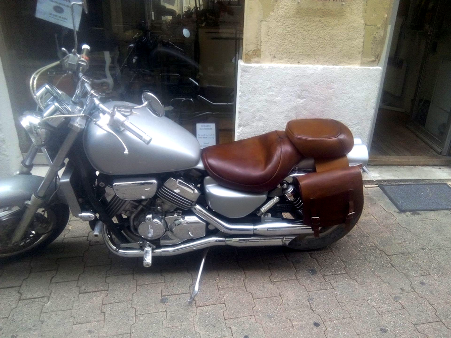 Moto argentée avec selle en cuir marron garée sur un trottoir à côté d'un bâtiment
