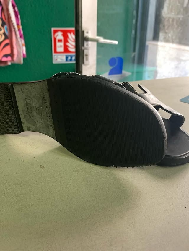 Sandale noire posée sur une table verte, à côté d'une poignée de fenêtre et de porte.