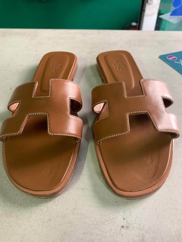 Une paire de sandales en cuir marron à larges brides, posées sur une table légère.