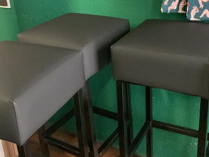 Deux tabourets de bar gris à pieds en métal noir contre un mur vert