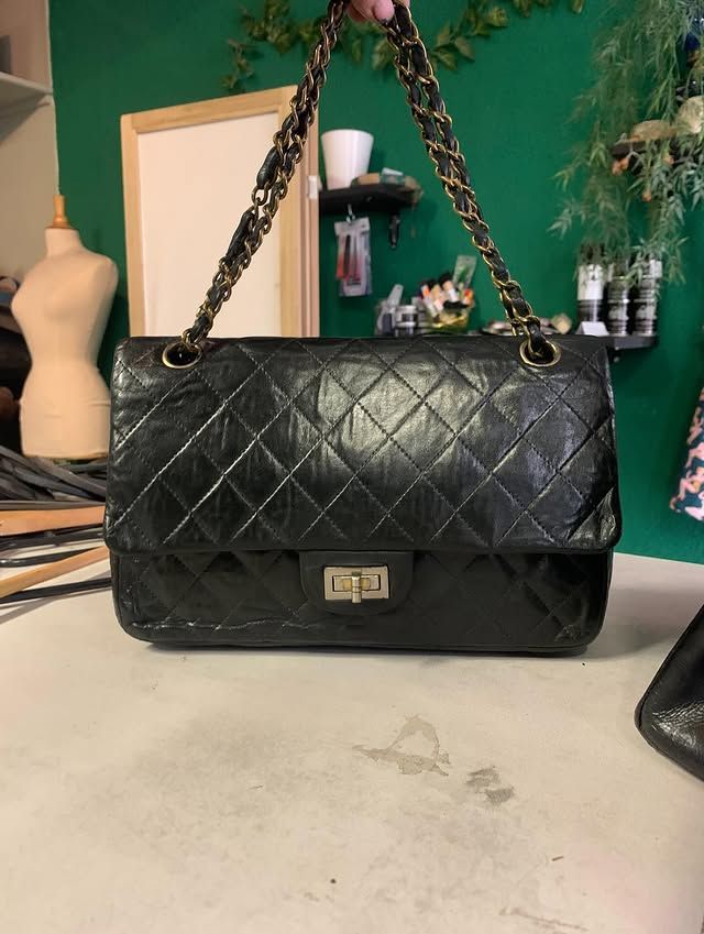 Sac à main matelassé noir à bandoulière chaîne dorée posé sur une table, avec des étagères et des éléments de décoration en arrière-plan.