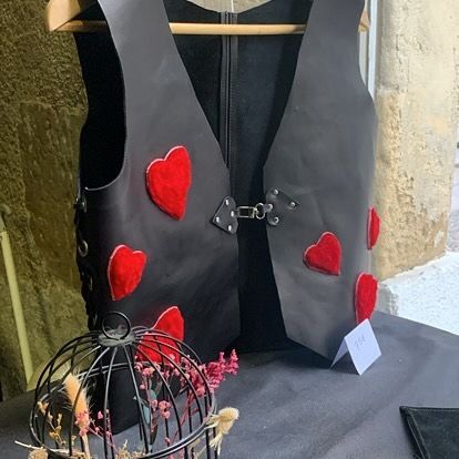 Un gilet noir orné de cœurs rouges à côté d'une petite cage à oiseaux sur une table