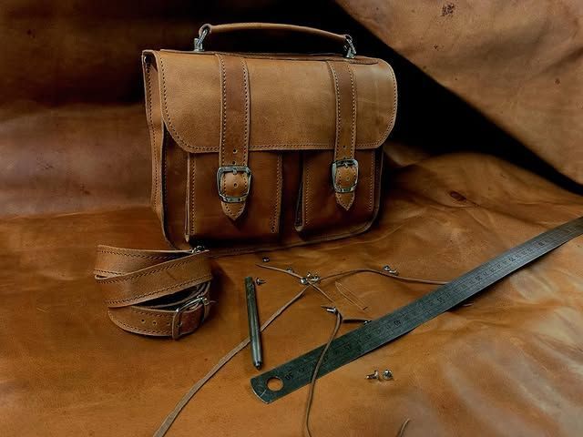 Sacoche en cuir marron avec bandoulière et petits accessoires sur une surface en cuir marron