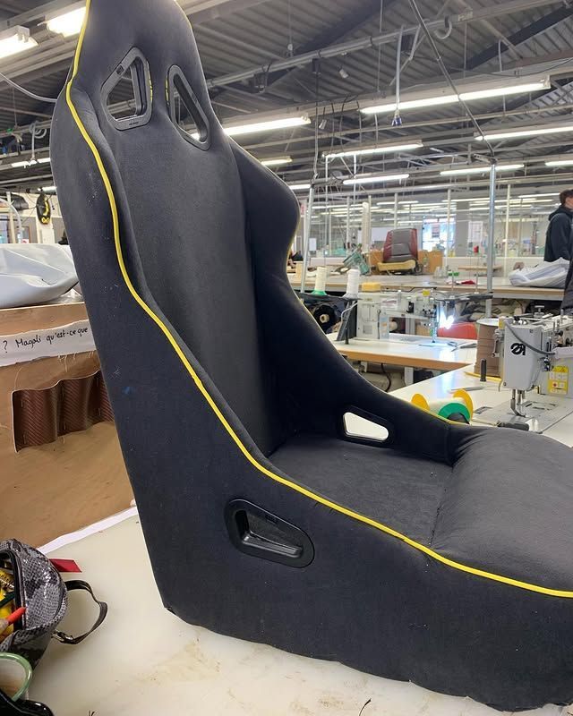 Siège de course noir avec passepoil jaune dans un atelier, vu de côté