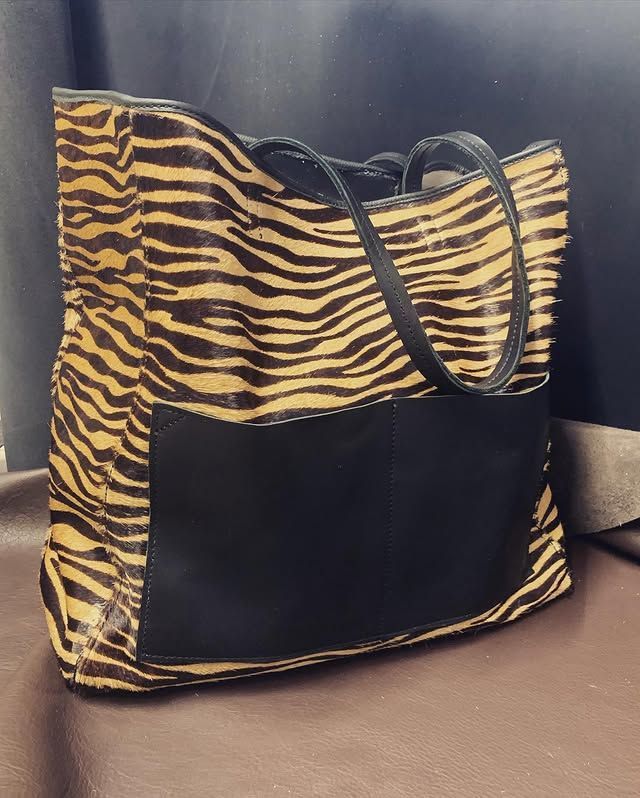 Un sac cabas à imprimé tigre avec panneau avant et anses noirs, posé sur un canapé.