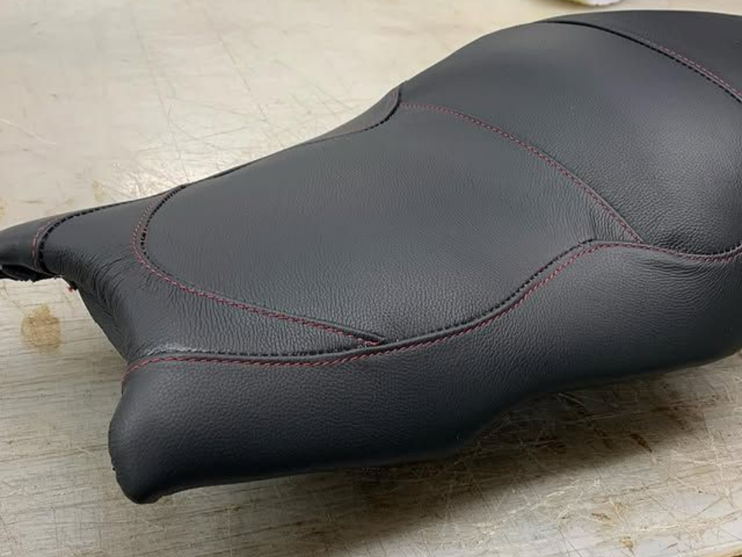 Selle de moto noire avec surpiqûres rouges sur un sol clair