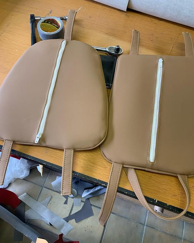 Deux coussins beiges rembourrés avec des coutures centrales blanches sont posés sur une table de travail, entourés de sangles et d'outils.