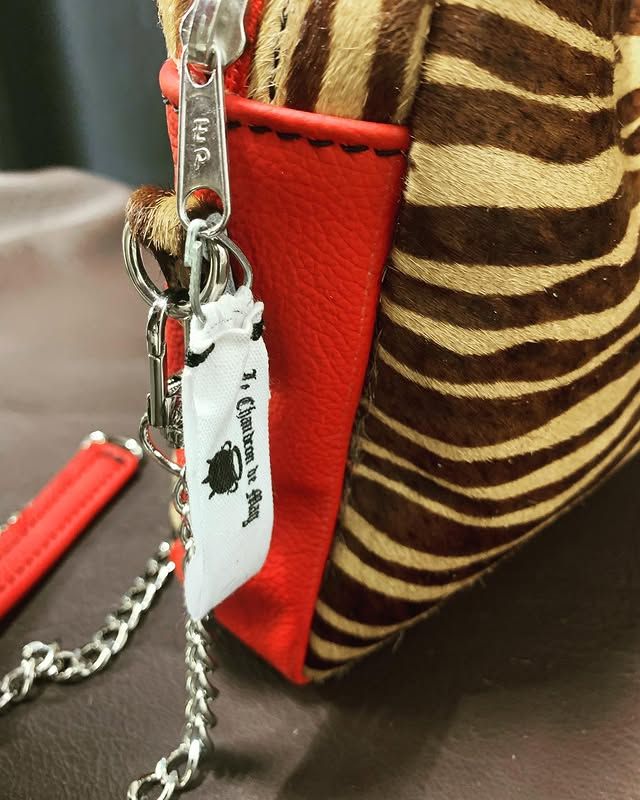Gros plan sur un sac à imprimé zèbre avec bordure rouge, chaîne argentée et étiquette blanche.
