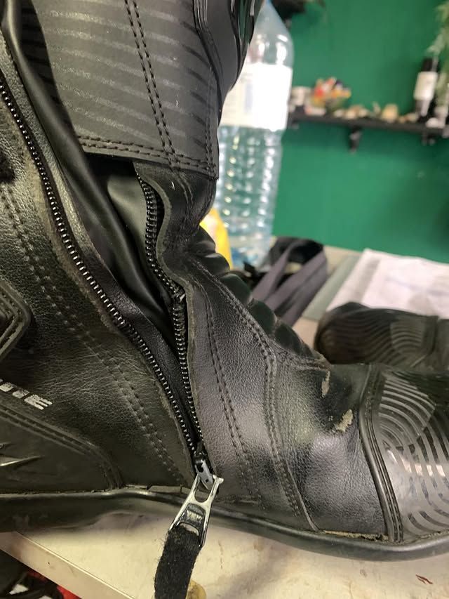 Gros plan d'une botte de moto noire à fermeture éclair posée sur une table verte, avec une bouteille d'eau en arrière-plan.