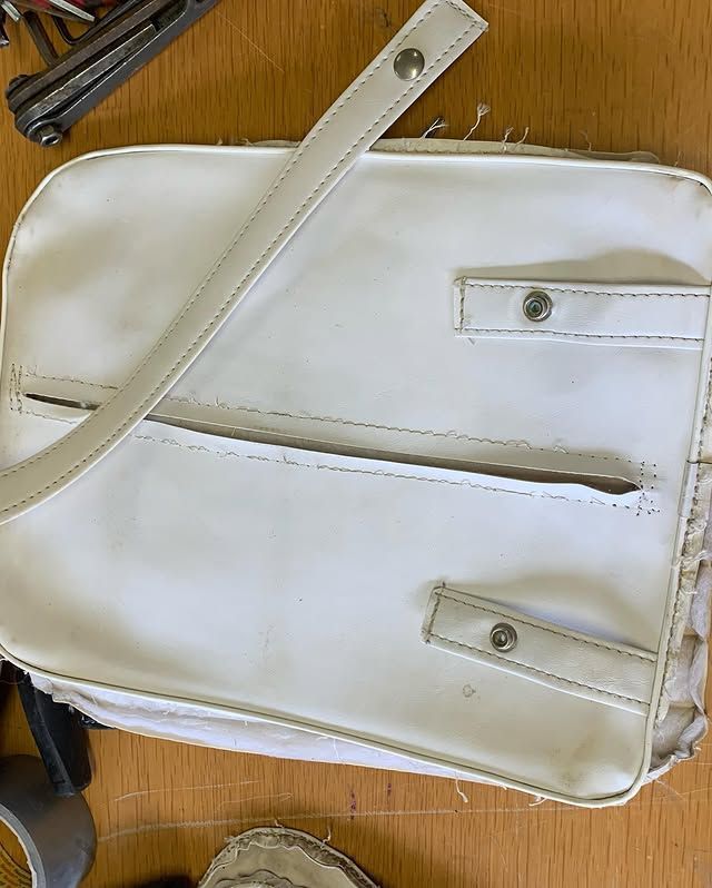 Sac à main blanc à bandoulière longue et boucles métalliques posé sur un sol en bois