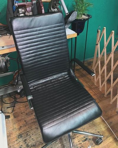 Fauteuil de bureau en cuir noir dans une pièce avec parquet et mur turquoise.