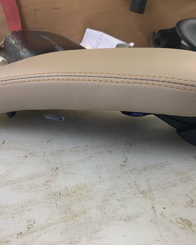 Gros plan sur un coussin beige incurvé aux coutures apparentes, posé sur un bureau blanc usé.