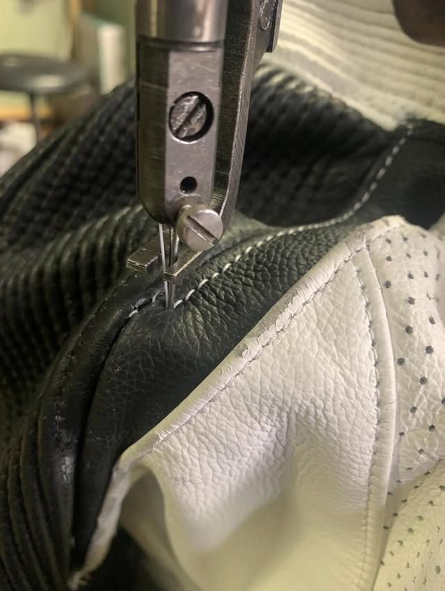 Gros plan sur une machine à coudre réalisant une couture en cuir noir et blanc.