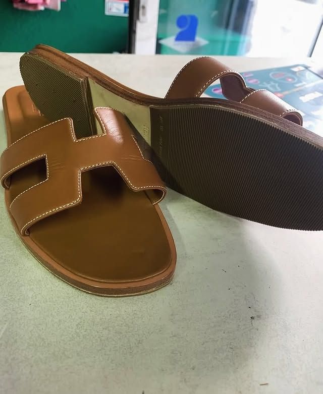 Deux sandales à talons marron posées sur une table, l'une montrant la semelle et l'autre les brides supérieures.