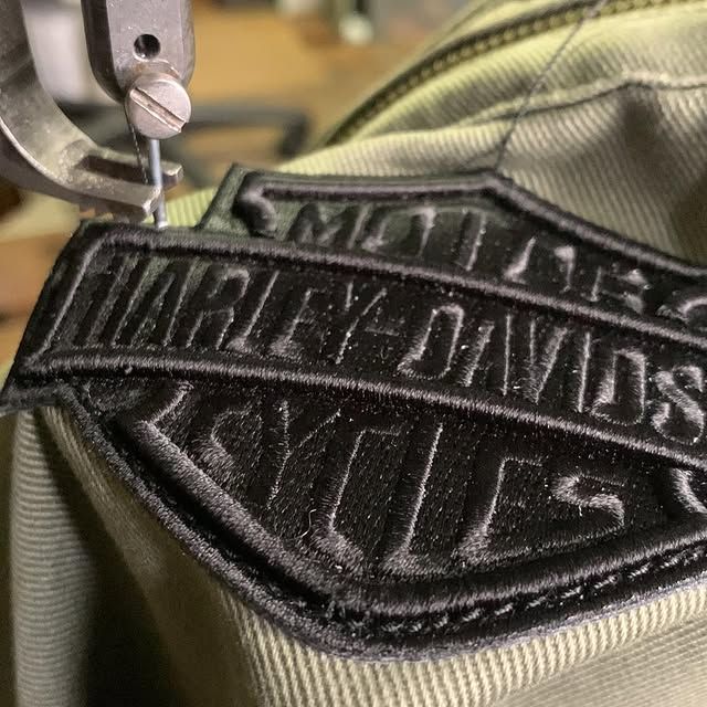 Une machine à coudre cousant un écusson noir Harley-Davidson sur un tissu beige.