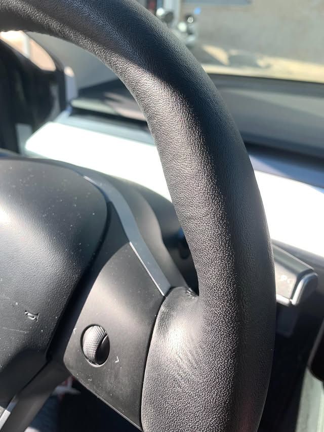 Gros plan sur un volant de voiture au soleil, montrant la jante noire texturée et le tableau de bord.