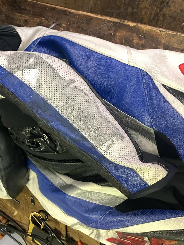 Combinaison de moto froissée sur une surface, laissant apparaître partiellement un objet noir à l'intérieur.