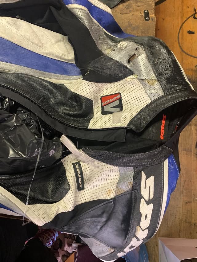 Des blousons de moto noirs, gris et bleus pliés sont empilés sur un plancher en bois.