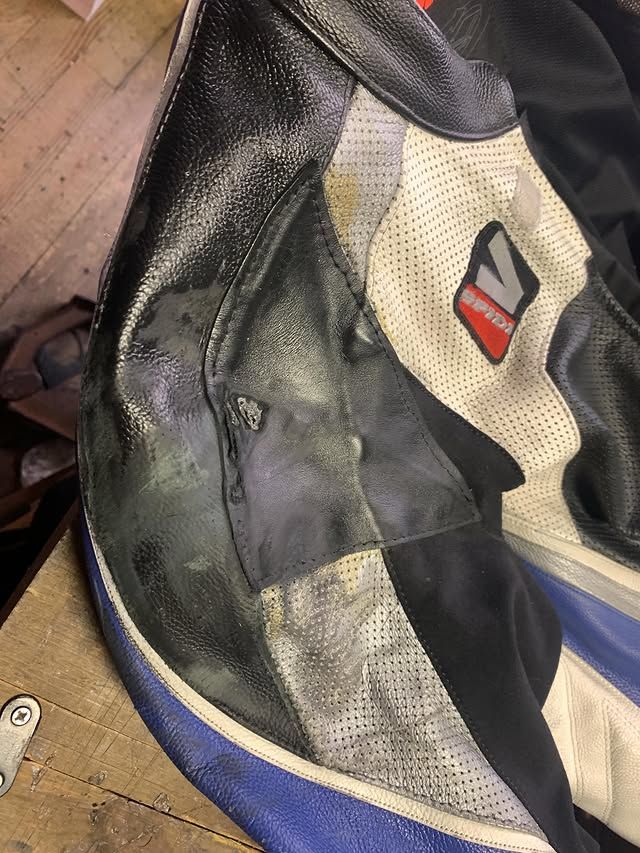 Gros plan sur une veste en cuir noir et beige usé, avec un logo rouge et blanc sur le côté.