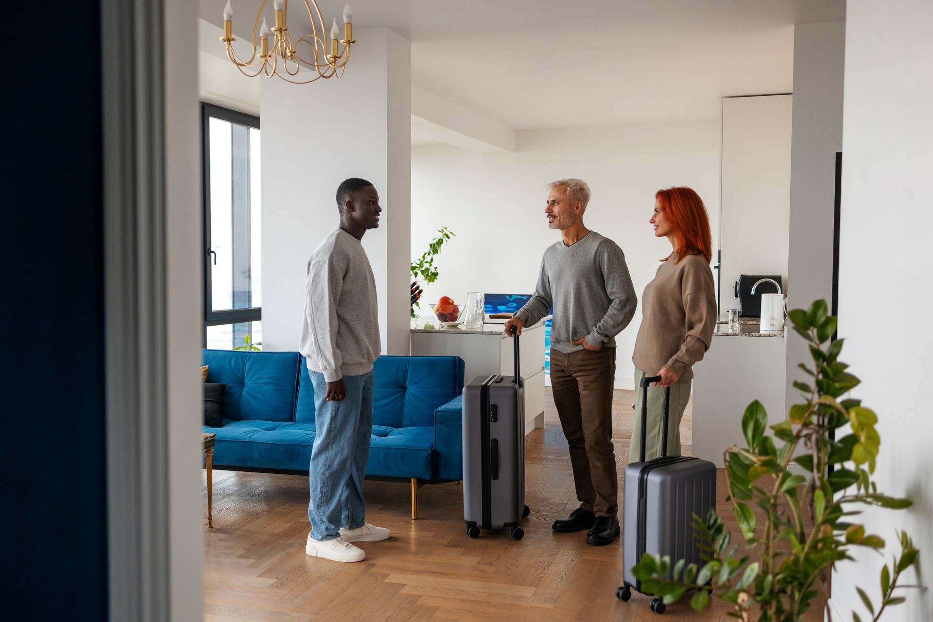 Man greets a couple with luggage in a modern apartment entryway.