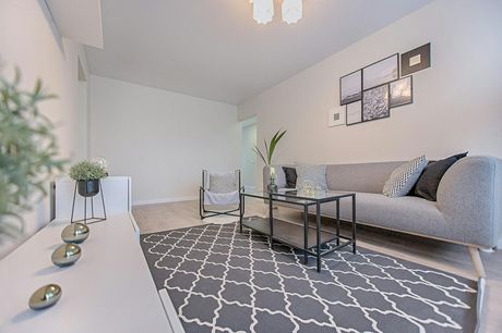 Modern living room with gray sofa, patterned rug, glass coffee table, and white console table